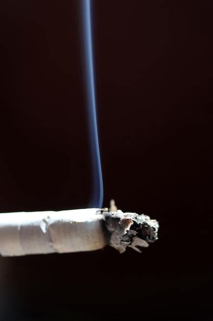 Detalhe de cigarro aceso fumaça contra fundo preto Foto Premium