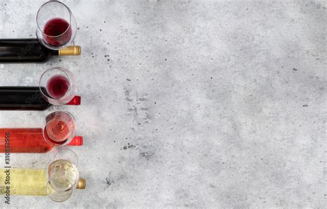 Different Wine Bottle And Wine Glasses With Bordeaux Red Rose And White On Concrete Background