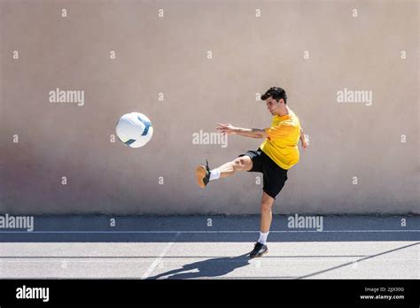 Young male player kicking football while practicing soccer against ...