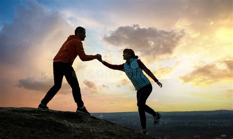 Man And Woman Hikers Helping Each Other To Climb Stone At Sunset In