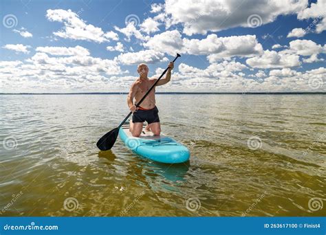 A Man Kneeling On A Sup Board With A Paddle In The Lake On A Sunny Day