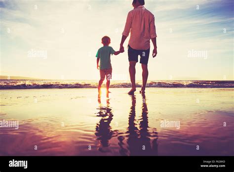 Father And Son Holding Hands Walking Together On The Beach At Sunset