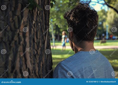 Back View Of Man Stalking Woman Hiding Behind Tree In Public Park With