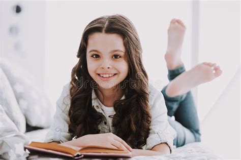 Petite Fille Mignonne Se Trouvant Sur Le Livre De Lit Et De Lecture