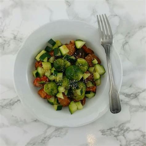 A White Bowl Filled With Cucumbers And Other Vegetables On Top Of A