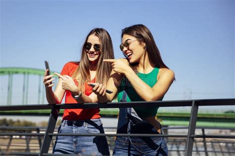 Smiling Young Best Female Friends Looking At Mobile Phone In The Park