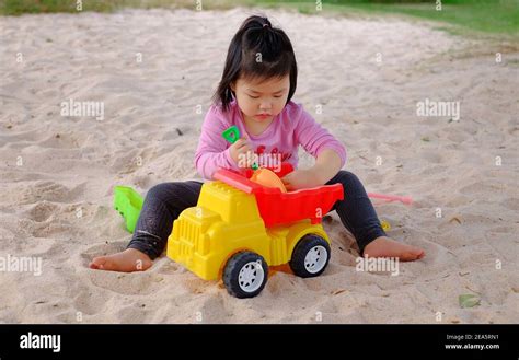 A Cute Young Asian Girl Playing With Colorful Plastic Toys And Sand In