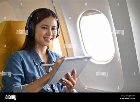 Beautiful Young Asian Female With Wireless Headphones Using Portable Digital Tablet On The Plane