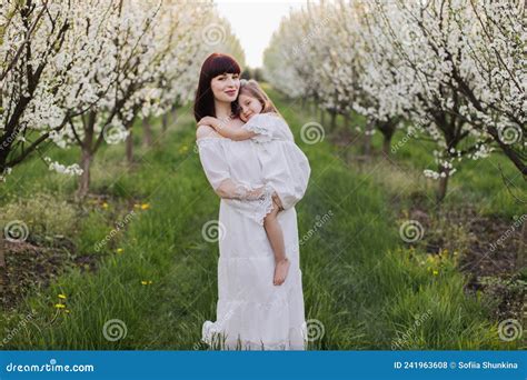 Mother Holding Her Daughter While Posing Among Spring Garden Stock