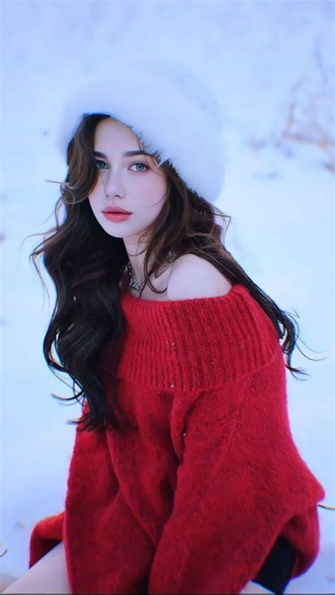 A Woman Wearing A Red Sweater And White Hat Sitting In The Snow With Her Hands On Her Hips