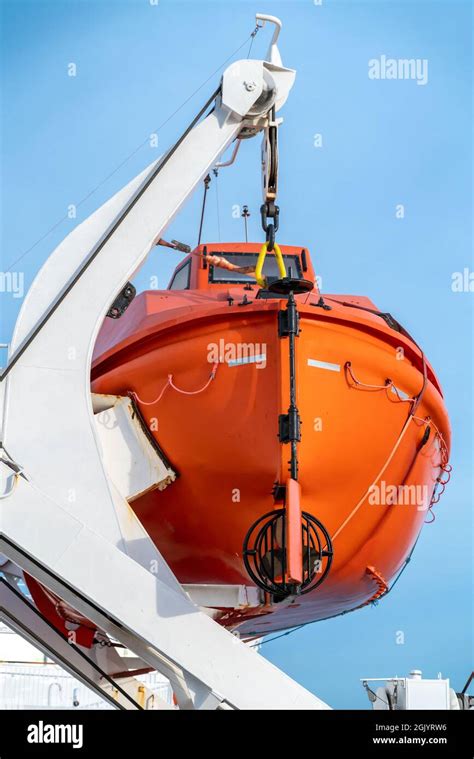 Vertical Shot Of Orange Life Boat Hanging On A Crane Onboard Sailing