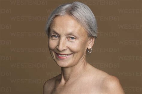 Portrait Of Naked Senior Woman With Grey Hair In Front Of Brown