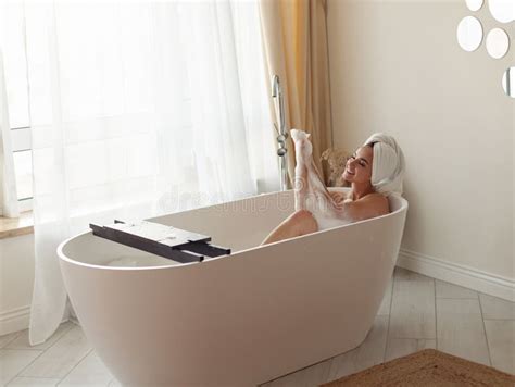 Caucasian Beautiful Woman Lying In Bathtub With Foam Taking Bath In Modern Bathroom Rubbing Legs