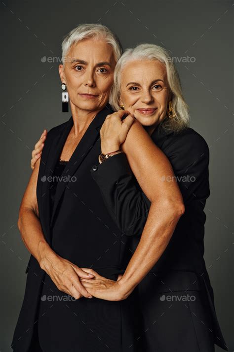 joyful senior woman in black attire embracing elegant female friend on ...