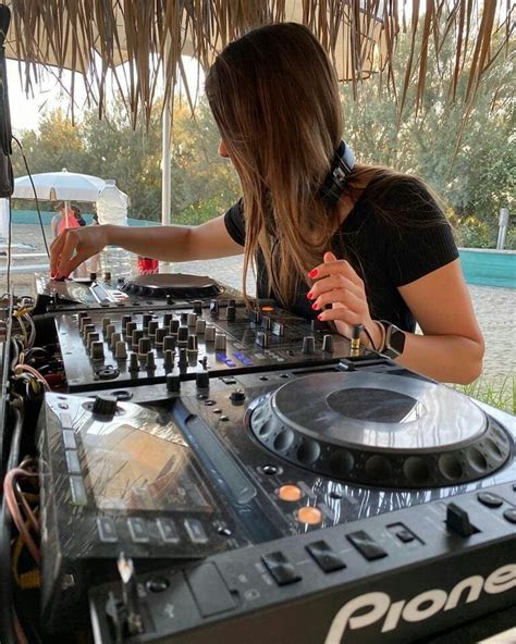 A Woman That Is Standing In Front Of A Dj S Set Up With Headphones On