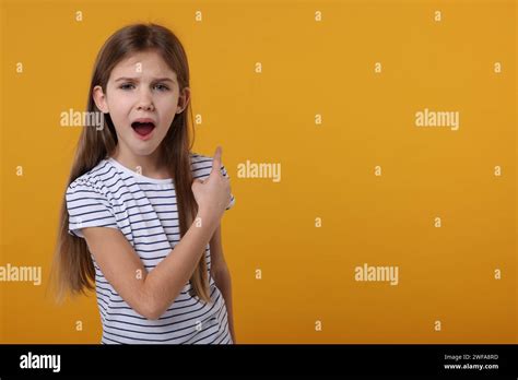 Surprised Girl Pointing At Something On Yellow Background Space For