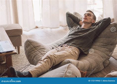 Handsome Teenage Guy Relaxing On Modern Soft Couch At Home In Living