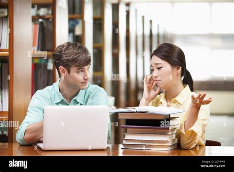 Two College Students Talking At Library While Studying Together Stock