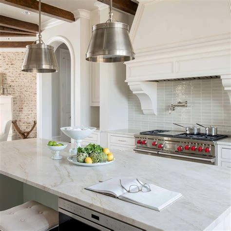 A White Kitchen With Marble Counter Tops And Stainless Steel Pendants