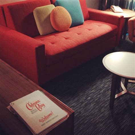 A Red Couch Sitting In A Living Room Next To A Table With A Book On It