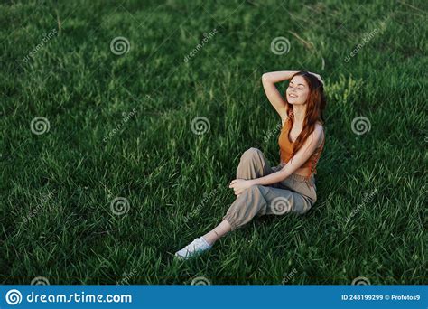 A Woman Enjoying The Outdoors Sitting In The Park On The Green Grass In Her Casual Clothes Lit