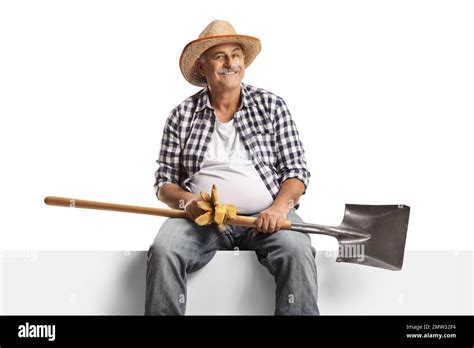 Cheerful Mature Farmer Sitting On A Blank Panel With A Shovel And