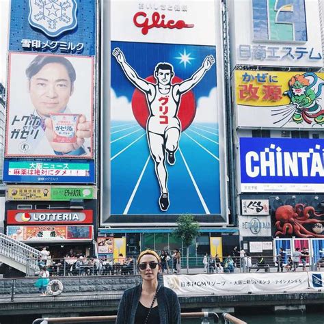 A Woman Standing In Front Of A Building With Many Billboards On It S Sides