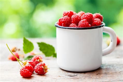 Premium Photo Fresh Raspberries In White Enamelled Mug On Table Outdoors