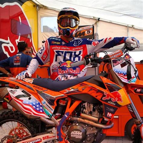 A Man Standing On Top Of An Orange Dirt Bike