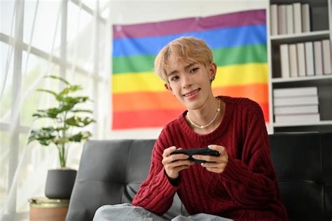 Premium Photo A Smiling Young Asian Gay Man Sits On A Sofa With His Smartphone In His Hands