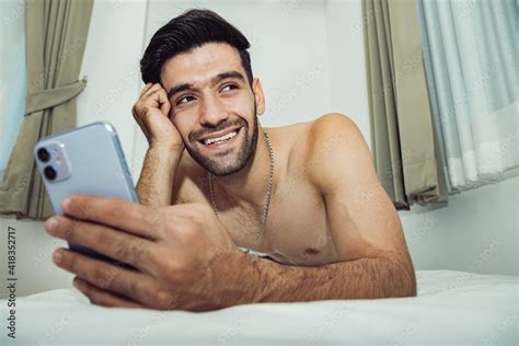 Handsome Shirtless Man On Bed With Intense Face Expression Using Mobile