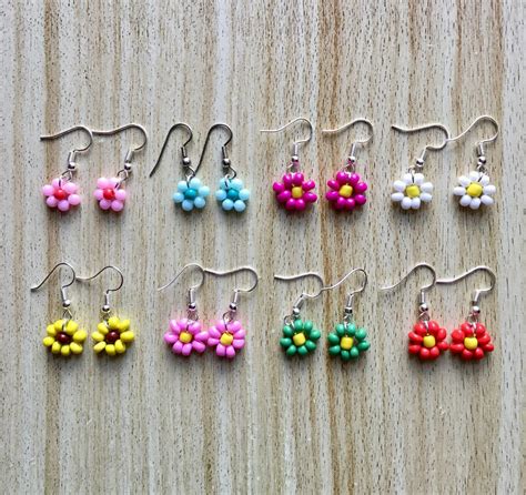 Small Flower Earrings Are Displayed On A Wooden Surface With The Word