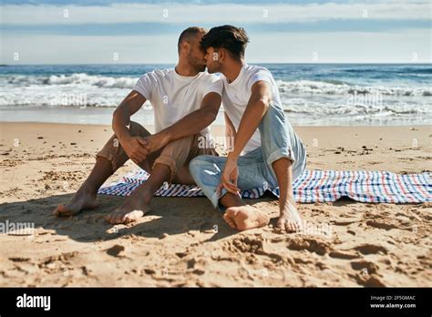 Un jeune couple gay s embrasse assis à la plage Photo Stock Alamy