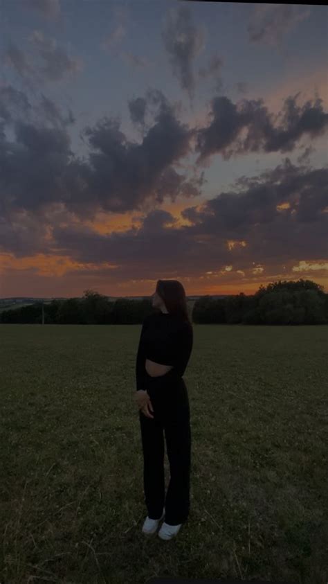 A Woman Standing In The Middle Of A Field At Sunset