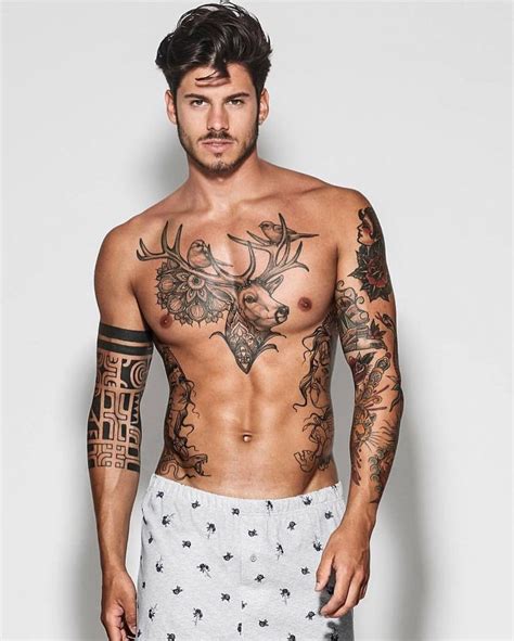 A Shirtless Man With Tattoos On His Chest And Arms Standing In Front Of