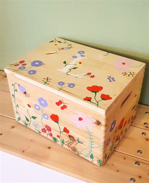 A Wooden Box With Flowers Painted On It Sitting On The Floor Next To A Wall