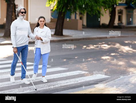 young woman helping senior blind man  cross road  city stock photo