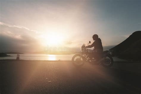 Silueta De La Moto En El Camino Durante Puesta Del Sol Foto De Archivo