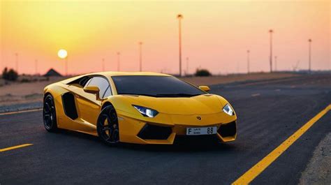 A Yellow Sports Car Is Driving Down The Road With The Sun Setting In