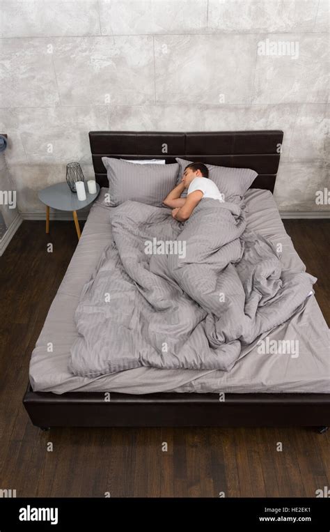 Young man sleeping alone in stylish bed with grey colors and bedside ...