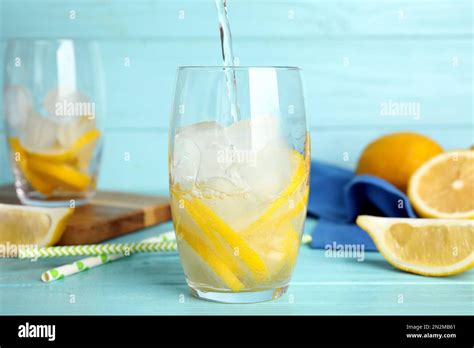 Pouring Soda Water Into Glass With Lemon Slices And Ice Cubes At Light