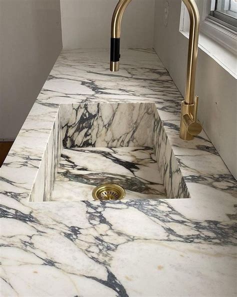 A Marble Sink With Gold Faucet Handles In A White And Black Bathroom Area