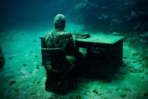 A Statue Is Sitting At A Desk In The Middle Of The Sea Floor With An