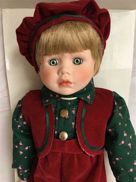 A Doll With Blonde Hair And Green Eyes Wearing A Red Outfit On A White