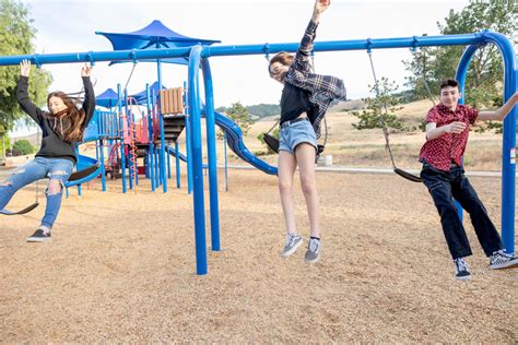 three older kids jumping off swings at a playground in San Jose