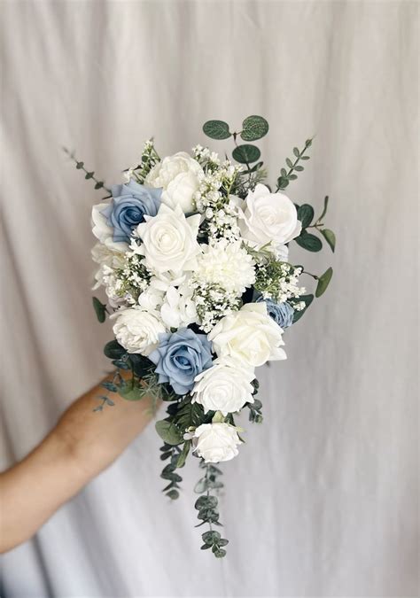 A Bouquet Of White And Blue Flowers In Someone S Hand On A White Background