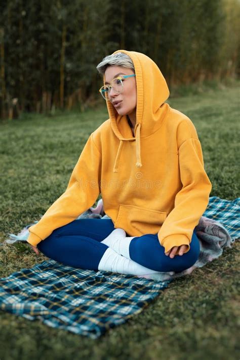 Cute Girl With Glasses In An Orange Hoodie Is Sitting In A Park In