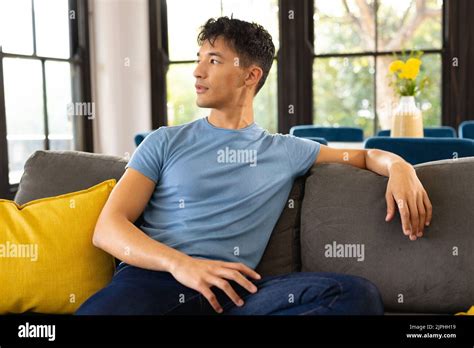 Happy Biracial Man Sitting On Sofa In Living Room Looking Away Stock