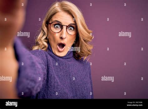 Middle Age Beautiful Blonde Woman Wearing Sweater And Glasses Make Selfie By The Camera Scared