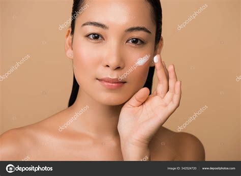 Beautiful Naked Asian Girl Applying Facial Cream Isolated Beige Stock